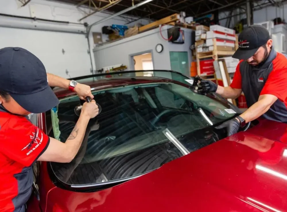 Technicians fitting a new windshield to a red car