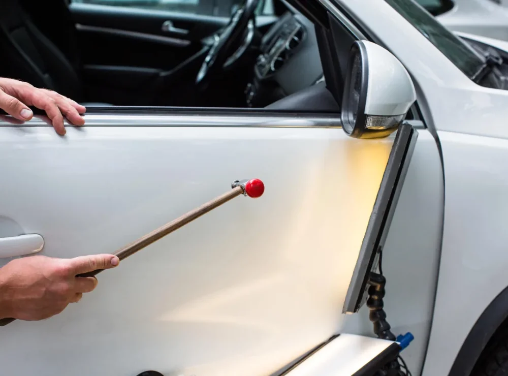 Technician removing a dent from a white car door with a PDR tool